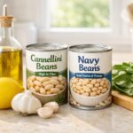 Bright kitchen counter with canned white beans (cannellini and navy), fresh garlic, lemon, olive oil, and leafy greens in natural light