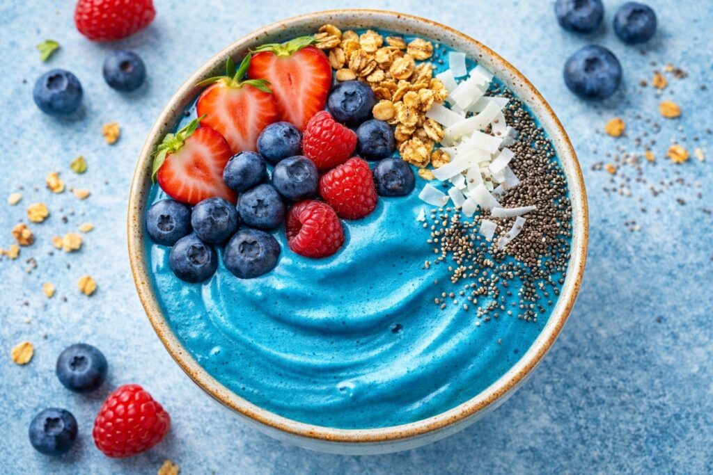 Vibrant blue spirulina smoothie bowl topped with berries, granola, coconut flakes, and chia seeds