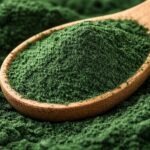 Fine green spirulina powder in a wooden spoon showing dark green color and smooth texture