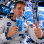 Astronaut drinking a blue spirulina smoothie inside the International Space Station with Earth visible through the window.