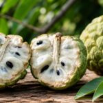 Ripe Annona squamosa (sugar apple) cut in half showing creamy white flesh and black seeds on a rustic wooden table.