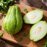 Fresh whole and sliced chayote squash showing white flesh and seed on a wooden cutting board