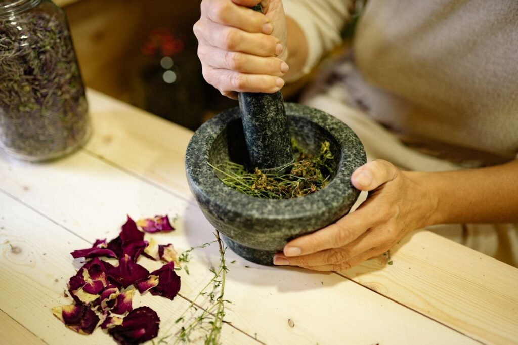A person grinding herbal ingredients in a stone mortar and pestle with dried petals nearby. Herb Synergy Calculator