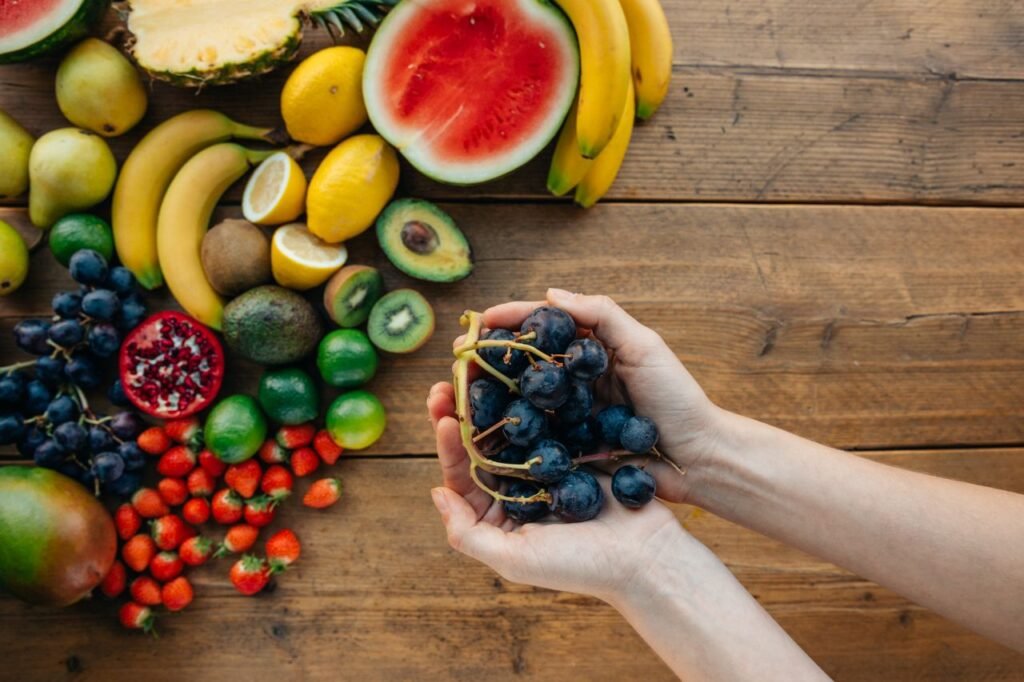 BMI calculator - A variety of fresh, organic fruits with hands holding grapes on the wooden table 